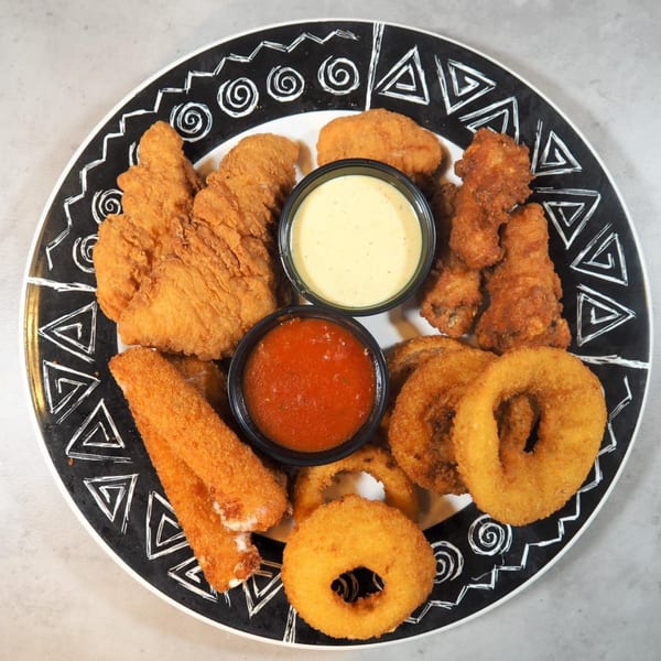 A black and white patterned plate filled with fried chicken tenders, wings, mozzarella sticks, and onion rings.