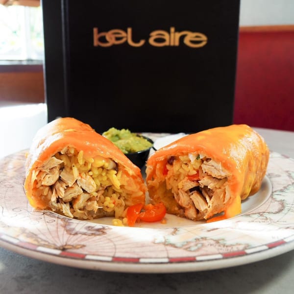 Two halves of a chicken and rice burrito with melted cheese, served with guacamole and sour cream.