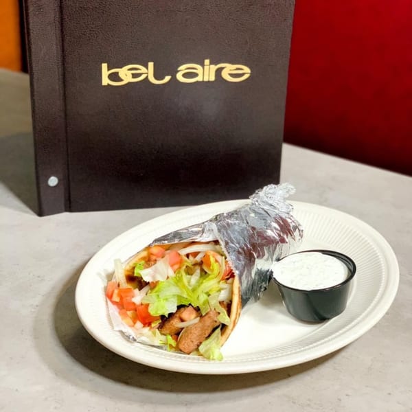 A Bel Aire Diner menu stands behind a gyro with lettuce, tomato, and a side of sauce.