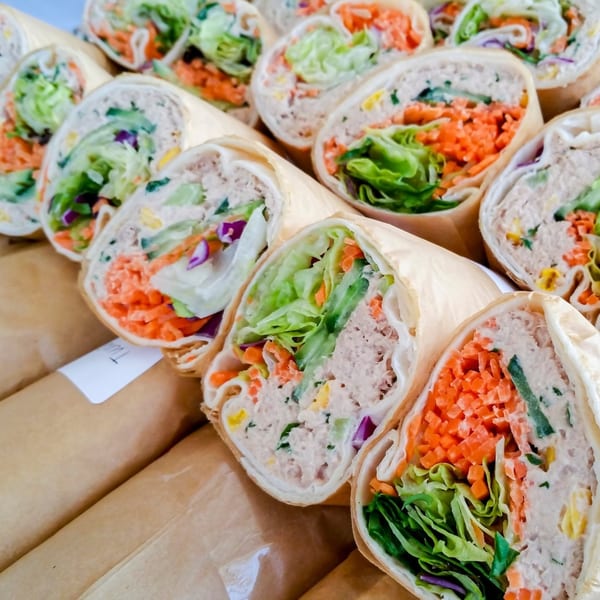 Rows of tuna salad wraps with lettuce, shredded carrots, and purple cabbage, individually wrapped in paper.