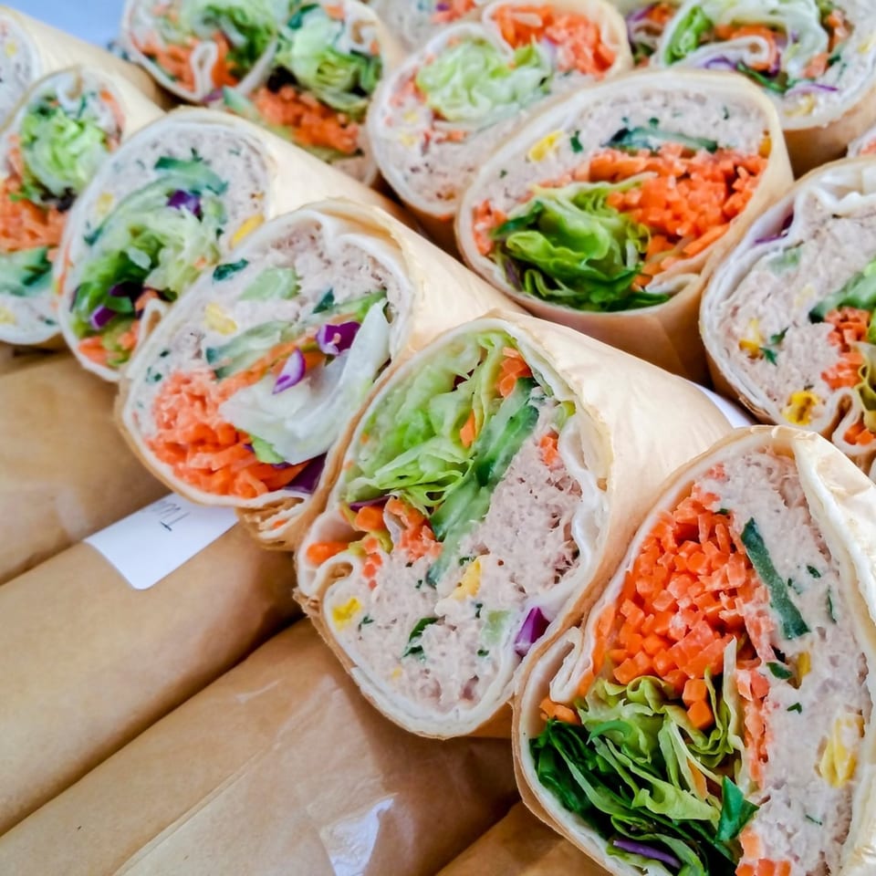 Rows of tuna salad wraps with lettuce, shredded carrots, and purple cabbage, individually wrapped in paper.