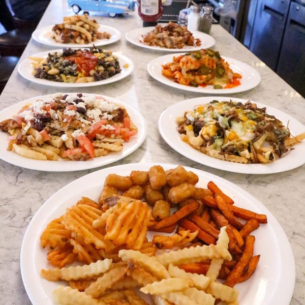 A diner counter displays various loaded fries, including waffle, sweet potato, and tater tots.